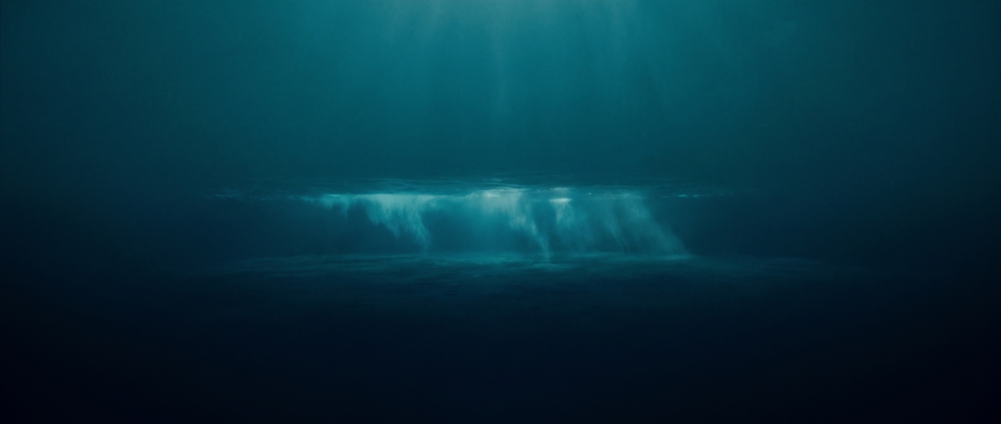 A lone surfer heading into a vast ocean at first light